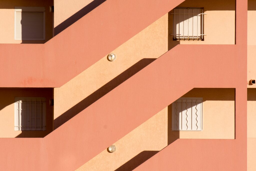 Façade rose rythmée par des lignes architecturales, des fenêtres et des jeux d'ombres